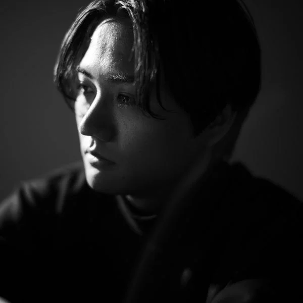 強い光と影が特徴的なモノクロポートレート。若い男性の横顔が捉えられ、思慮深く、どこか憂いを帯びた表情が印象的です